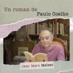 Jean Marc Malzac assis dans un fauteuil ancien, devant une bibliothèque, il lit un roman de Paulo Coelo.